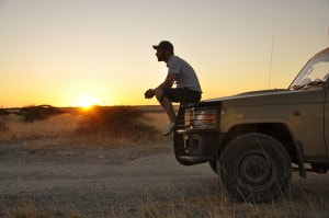 Sunset with a man sitting on the front bumper of a jeep